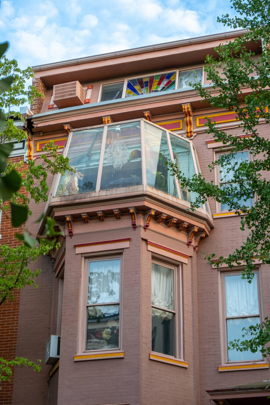 The top of a colorful pink house with red and yellow accents. At the top is a sunroom filled with crystals and stuffed animals.